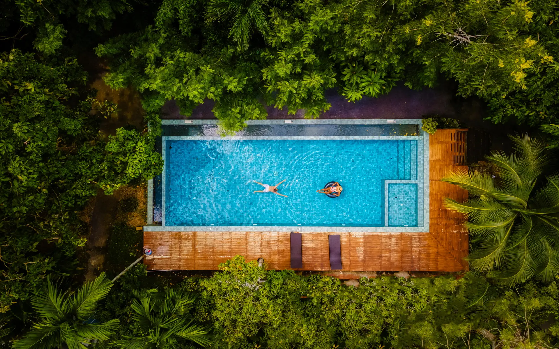 couple men and woman in swimming pool in the jungle of Krabi Thailand, aerial view with drone above