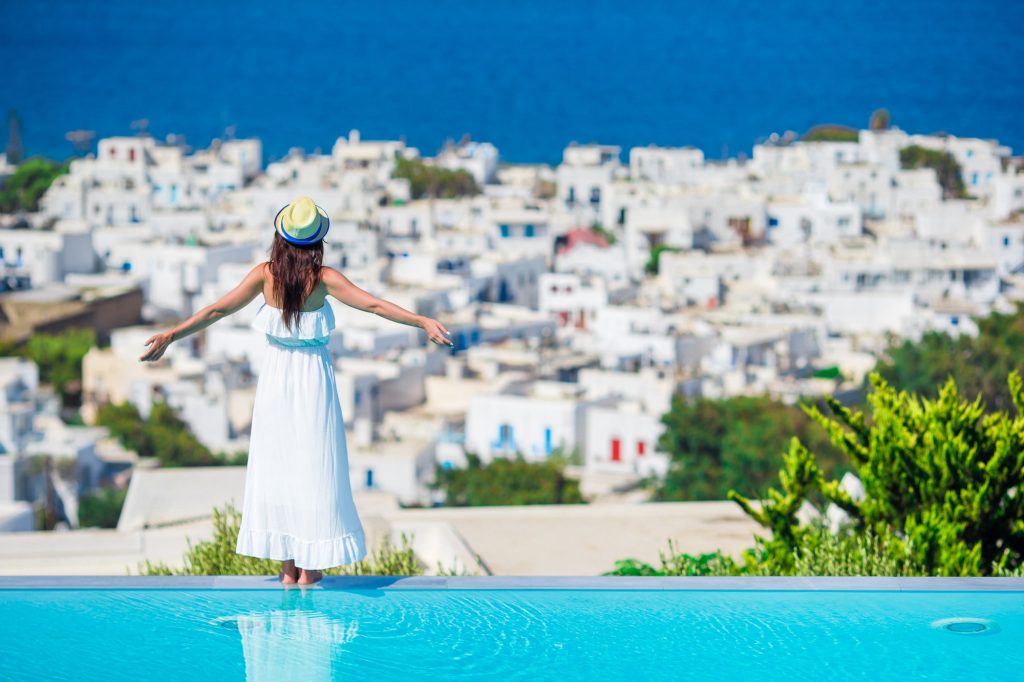 Beautiful young woman relaxing near pool with amazing view on Mykonos, Greece